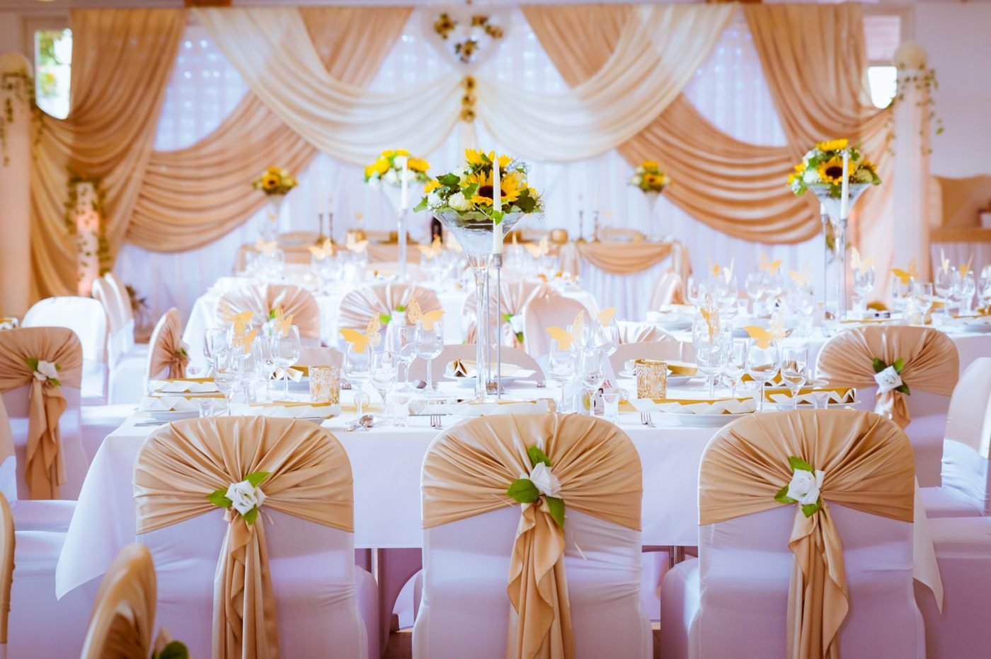 Hochzeitssaal in Gold mit drapiertem Stoffhimmel und Stuhlschleifen
